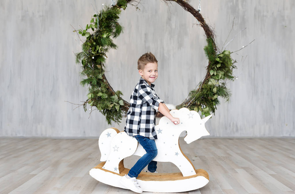 Schattige kleine jongen zat op een paard houten speelgoed in een interieur van studio. Horizontale portret - Foto, afbeelding