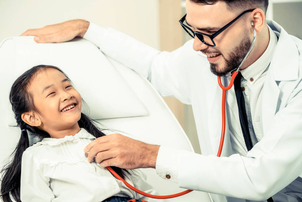 Young male doctor examining little kid in hospital office. The kid is happy and not afraid of the doctor. Medical children healthcare concept. - Фото, изображение