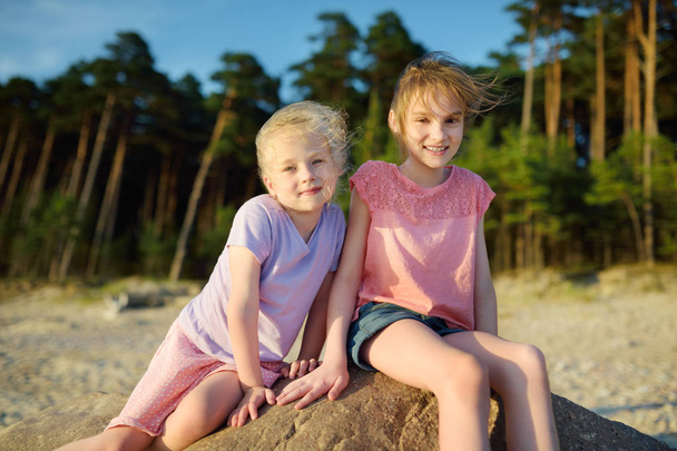 Two cute young sisters having fun on sandy beach on warm sunny summer day at sea - Fotoğraf, Görsel