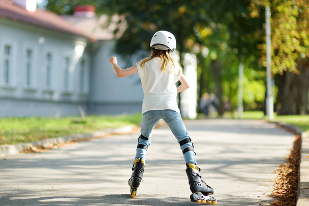 Pretty young girl learning to roller skate on beautiful summer day in a park - Valokuva, kuva