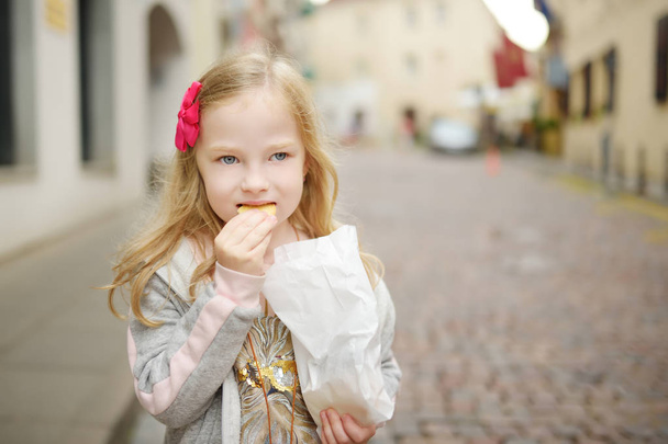 Adorable little girl eating fresh baked cookies on warm and sunny summer day in Vilnius, Lithuania - Foto, imagen