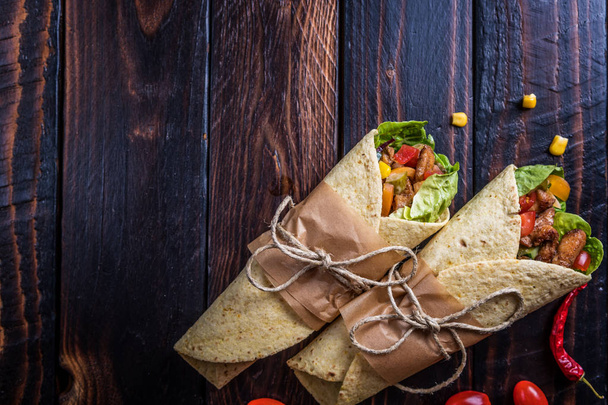 Traditional mexican tortilla wrap with vegetables and grilled chicken meat on dark wood table - Foto, immagini