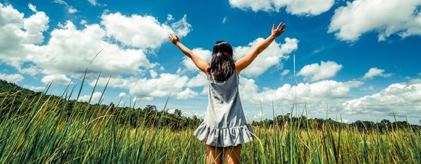 Young beautiful woman on green grass meadow spreading arms to the blue sunny sky on summer day. Getaway and meditation concept. - Photo, Image