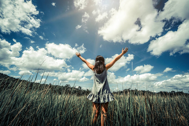 Joven mujer hermosa en el prado de hierba verde extendiendo los brazos al cielo azul soleado en el día de verano. Escapada y concepto de meditación
. - Foto, Imagen