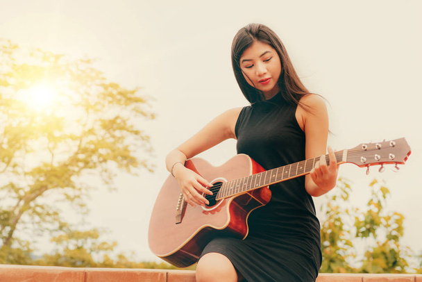 Ευτυχισμένη γυναίκα παίζει κιθάρα με φόντο φύση. Έννοια μουσική και χαλάρωση. - Φωτογραφία, εικόνα