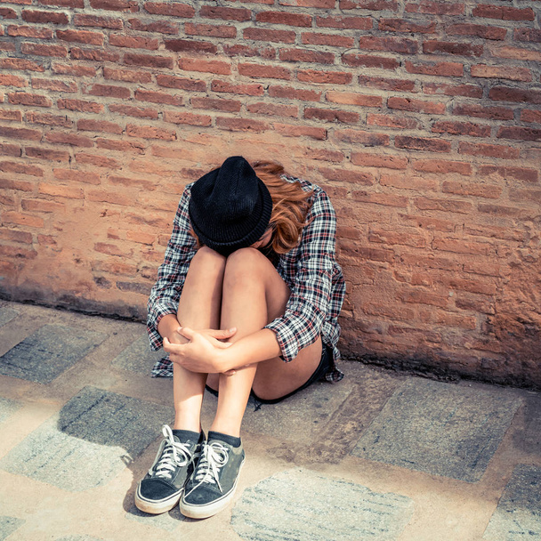 Depressed teenage woman feeling sad alone against brick wall in old town. Education and family failure concept. - Photo, Image