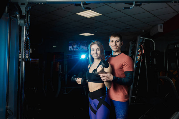 Aktif güzel fitness modeli kız pazı dumbbells ile birlikte spor salonunda bir eğitmen ile trenler. - Fotoğraf, Görsel