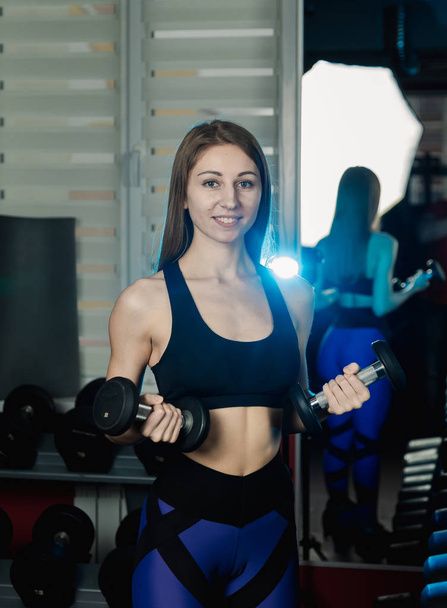 Young and beautiful woman working out with dumbbells in gym. Biceps curls. - Φωτογραφία, εικόνα