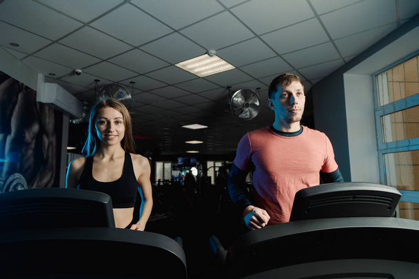 aktive schöne Fitness-Model Mädchen und athletische Mann trainieren auf dem Laufband in der Turnhalle. - Foto, Bild