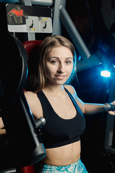 Active beautiful fitness model girl trains pectoral muscles on a simulator in the gym. - 写真・画像