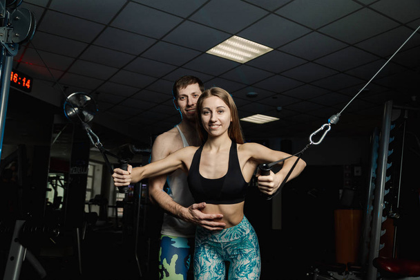 Active beautiful fitness model girl trains the pectoral muscles on the simulator along with a trainer in the gym. - Фото, зображення