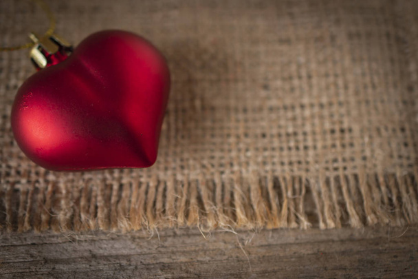 Κόκκινη πλαστική καρδιά τοποθετείται στο τσουβάλι και το ξύλινο τραπέζι. - Φωτογραφία, εικόνα