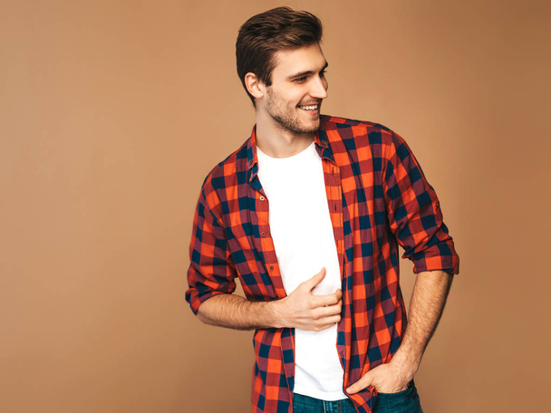 Portrait of handsome smiling stylish hipster lumbersexual businessman model dressed in red checkered shirt. Fashion man posing on golden background - Fotoğraf, Görsel