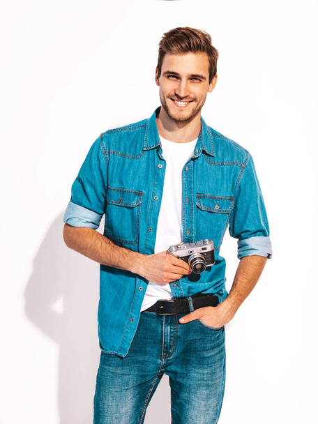 Portrait of handsome smiling man wearing summer hipster jeans clothes. Model male taking picture on old vintage photo camera. Isolated on white - Foto, Imagem