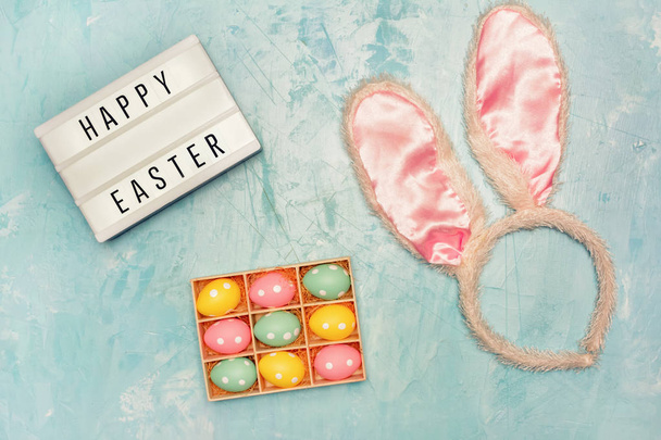 Modelo de cartão de Páscoa feliz com ovos pintados e penas e orelhas de coelho no fundo azul
  - Foto, Imagem