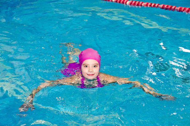 Portrait of cute smiling little girl child swimmer in pink swimming suit and cap in the swimming pool indoor - Photo, Image
