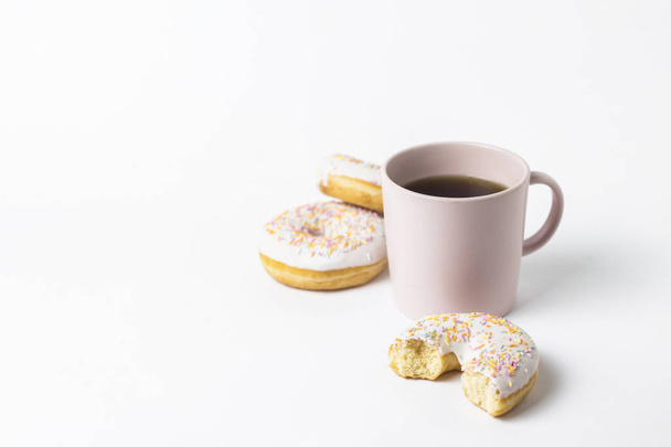 Roze kopje met koffie of thee en fris lekkere donuts, zoete veelkleurige decoratieve snoep op een witte achtergrond. Concept van de bakkerij, vers gebak, heerlijk ontbijt, fastfood - Foto, afbeelding