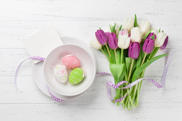 Easter greeting card with tulip flowers bouquet and easter eggs. Top view over white wooden table with space for your greetings - Fotografie, Obrázek
