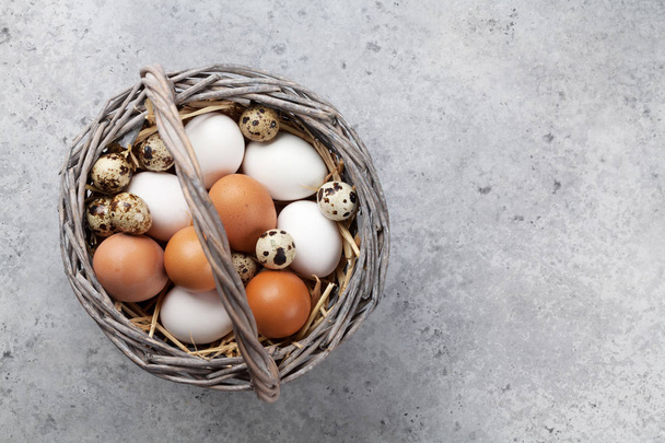 Kura i przepiórcze jajka w koszyku na stole z kamienia. Wielkanocne z życzeniami. Widok z góry z miejsca na życzenia - Zdjęcie, obraz