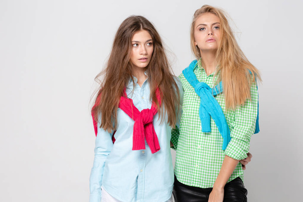 happy girlfriends women in shirts and a sweater on his shoulders. Fashion spring image of two sisters. Colorful colors clothes. Models with Blonde and light brown hair. Looking at camera . - Photo, Image