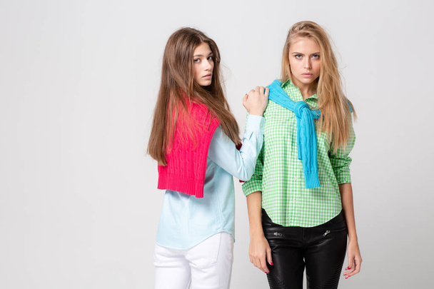 happy girlfriends women in shirts and a sweater on his shoulders. Fashion spring image of two sisters. Colorful colors clothes. Models with Blonde and light brown hair. - 写真・画像
