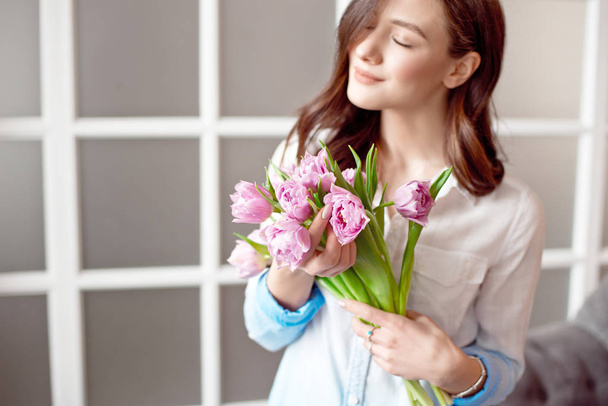 Close-up picture of a woman in white shirt showing a bouquet of spring flowers. Congratulations on the holiday - Photo, Image