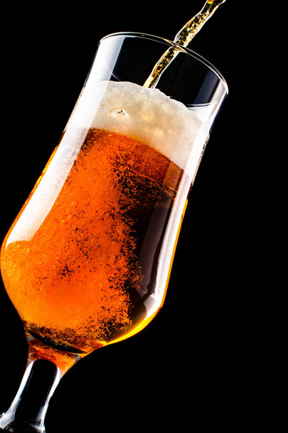 Beer is pouring into a glass from bottle isolated on black background - Photo, Image