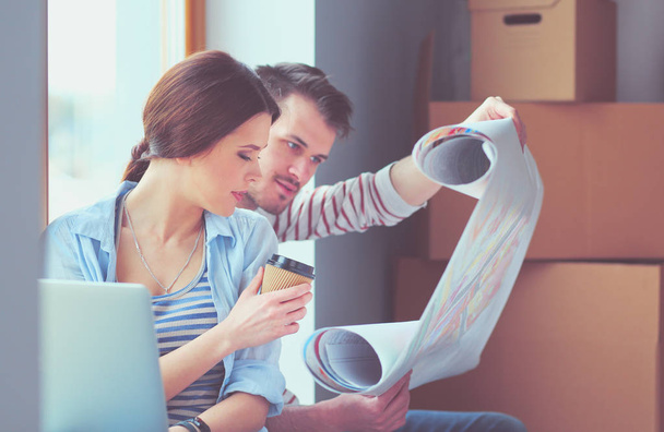 Young couple sitting on the floor and looking at the blueprint of new home. Young couple - Foto, Imagen