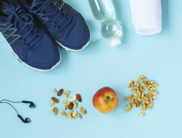 Sportovní boty, přeskakování lana, ořechy, sluchátka, apple a láhev vody na modrém pozadí. - Fotografie, Obrázek
