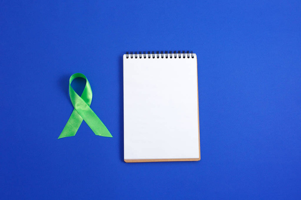 Işık mavi zemin üzerine yeşil şerit ve açık defter. Karaciğer kanseri lenfoma farkındalık. Sağlık ve tıp kavramı. - Fotoğraf, Görsel