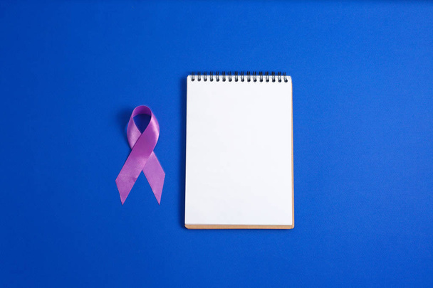 Paarse linten en open notitieblok op blauwe achtergrond, de ziekte van Alzheimer, Pancreatic kanker, epilepsie bewustzijn, bewustzijn van huiselijk geweld, - Foto, afbeelding