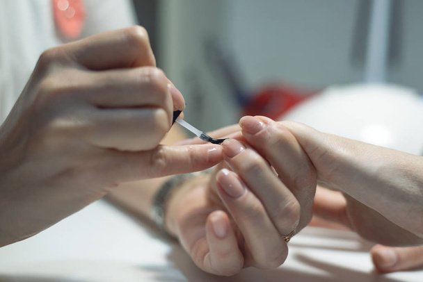 Manicurist is applying a nail base gel on a female finger nails. Nail care concept. - Photo, Image