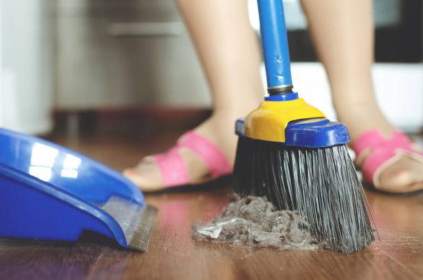 Woman is sweeping the floor by a sweeping brush from a dust. - Foto, imagen
