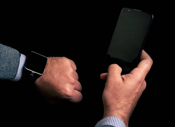 close up picture of man hands using smartphone and smartwatch with black background - 写真・画像