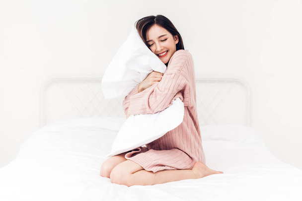 Красива жінка посміхається до камери і розслабляється з подушкою на ліжку в її кімнаті вдома
 - Фото, зображення