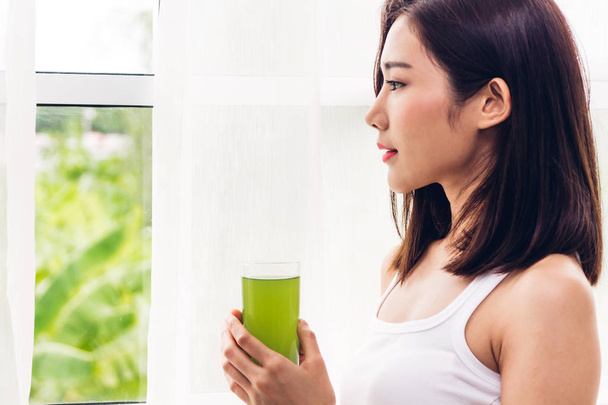 Kadın zevk home.dieting concept.healthy yaşam tarzı, oturma odasında pencere perdeleri yakınındaki sağlıklı içme yeşil detoks sebze suyu - Fotoğraf, Görsel