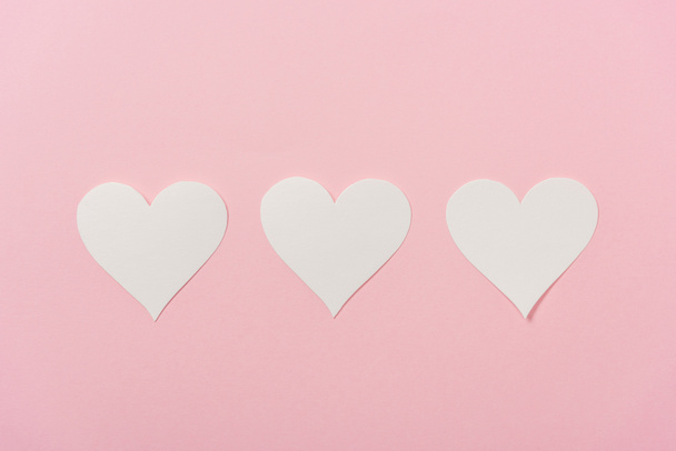 white paper hearts arranged in row on pink background - Φωτογραφία, εικόνα