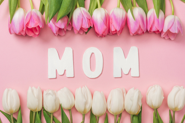 pink and white tulips arranged in rows with paper word mom in center on pink background - Foto, immagini