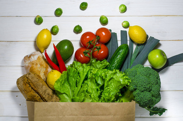 Бумажный пакет различных здоровых продуктов питания на белом деревянном фоне. Вид сверху
 - Фото, изображение