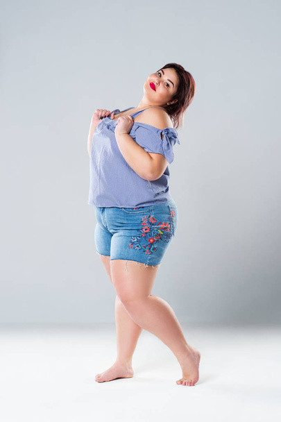 Plus size fashion model in jean shorts, fat woman on gray studio background, overweight female body - 写真・画像