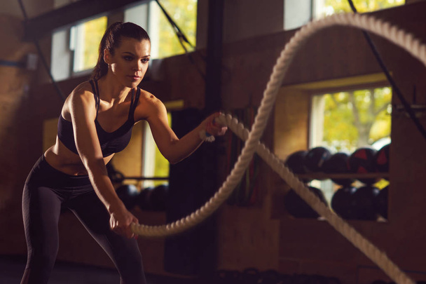 Fit, sporty and athletic sportswoman working in a gym. Woman training using battle ropes. Sports, athletics and fitness concept. - Foto, imagen