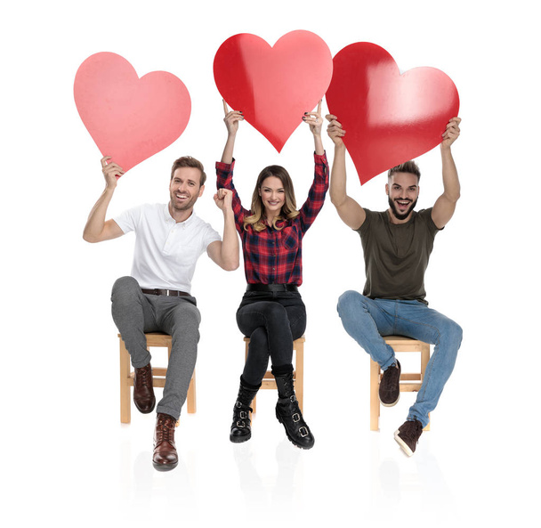 Три случайные люди с руками в воздухе празднуют любовь, держа большие красные сердца на День Святого Валентина на белом фоне
 - Фото, изображение