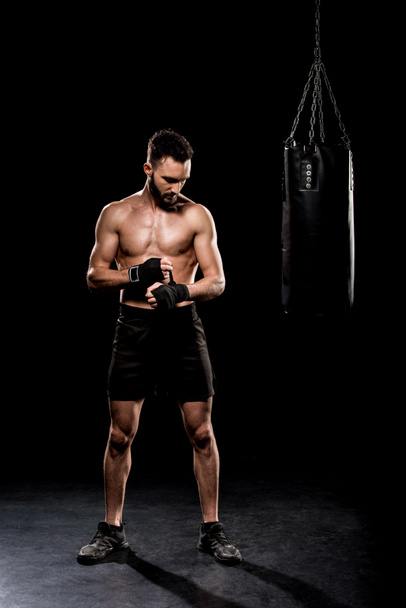 boxeador corto de pie cerca del saco de boxeo sobre fondo negro
 - Foto, Imagen