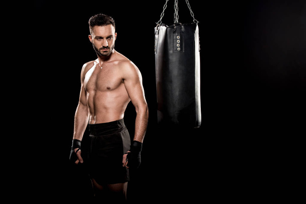 boxeador sin cortocircuito muscular mirando saco de boxeo aislado en negro
 - Foto, Imagen