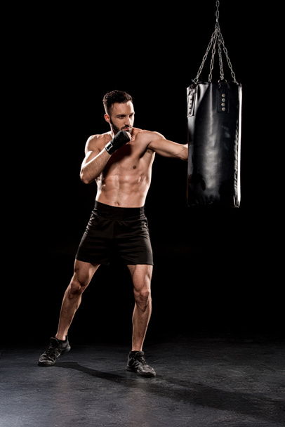 guapo barbudo boxeador ejercicio con saco de boxeo sobre fondo negro
 - Foto, Imagen