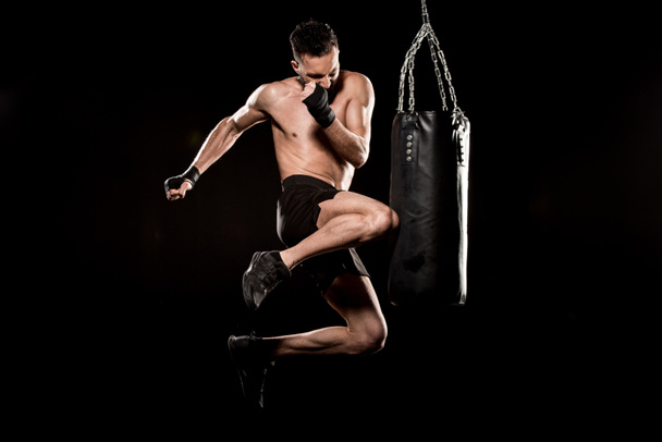 athlète sans short effectuant coup de pied volant près sac de poinçonnage isolé sur noir
 - Photo, image