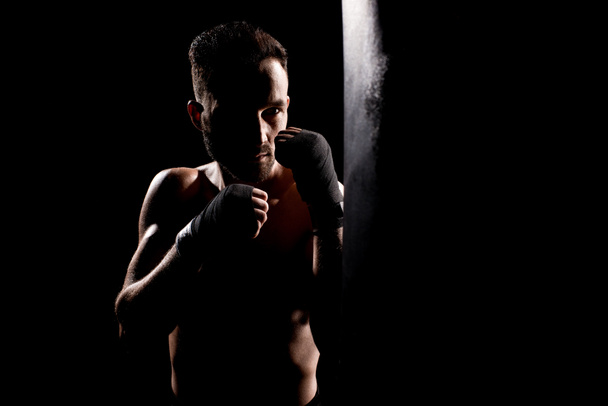 atleta sin cortocircuito golpeando saco de boxeo aislado en negro
 - Foto, Imagen