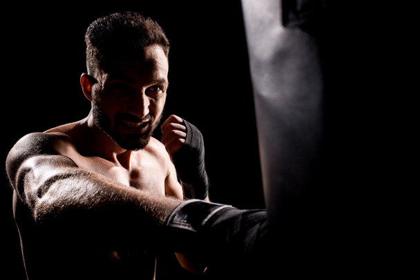 deportista sin cortocircuito golpeando saco de boxeo aislado en negro
 - Foto, Imagen