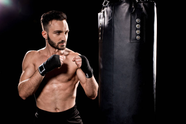 jóképű sportoló boksz jelent állandó és látszó-on boxzsák-fekete háttér - Fotó, kép