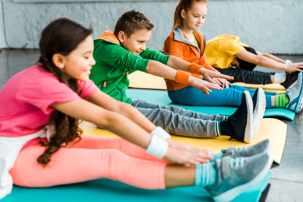 Kids in bright clothes stretching on fitness mats - 写真・画像